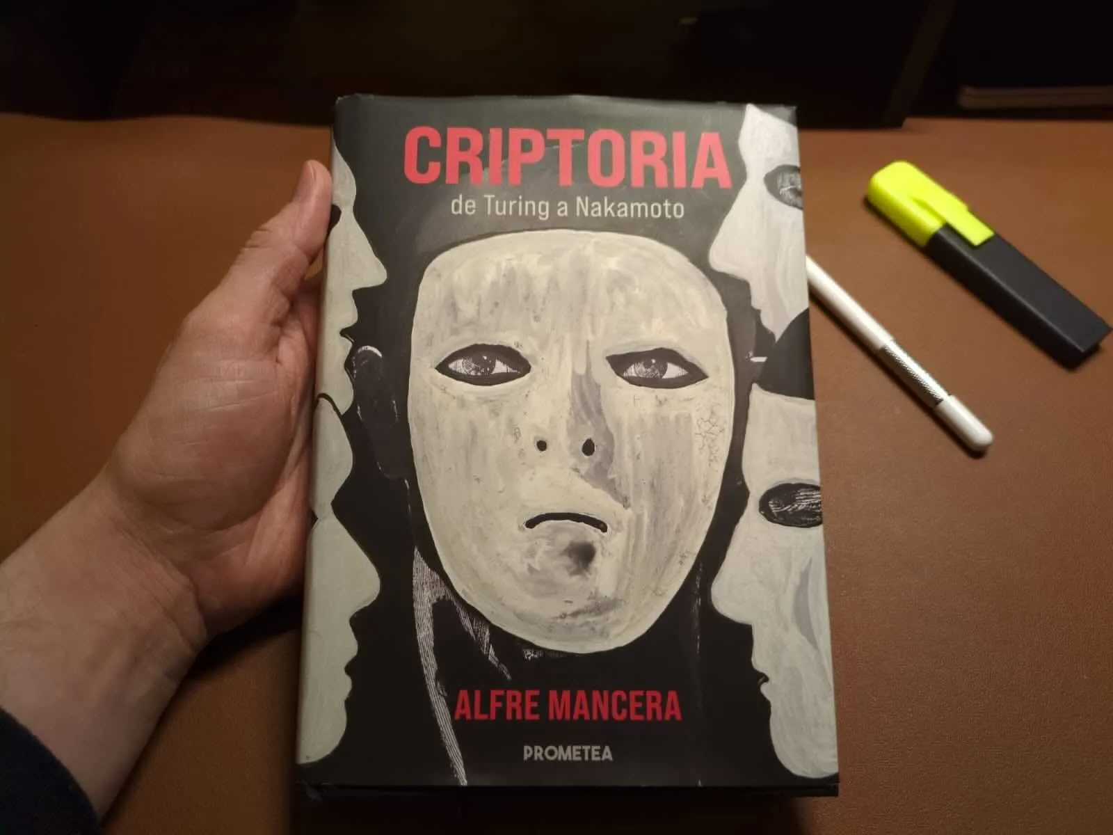 A hardback copy of Criptoria: de Turing a Nakamoto by Alfre Mancera, painted masks on the cover